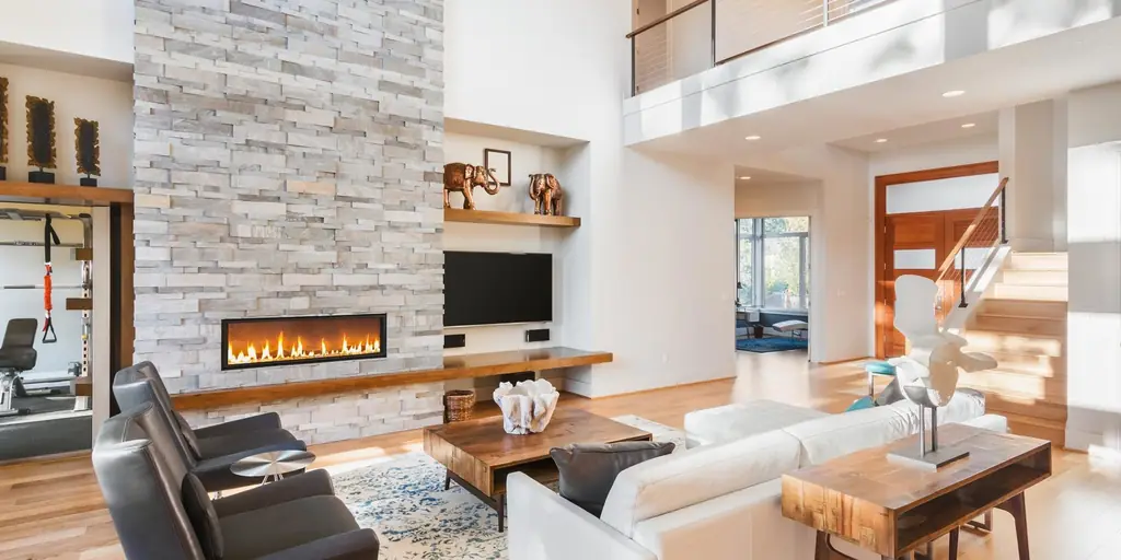 Bright living room with a floor-to-ceiling stone fireplace wall and open loft above