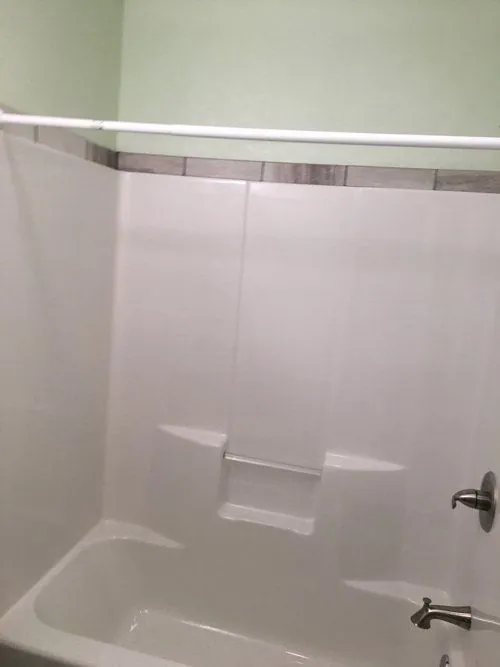 Bathtub with a white one-piece surround and shower valve