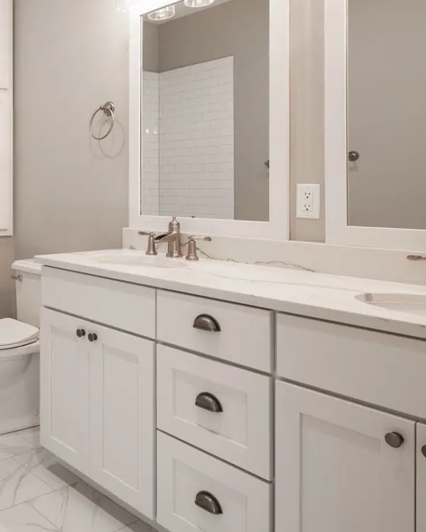 Remodeled bathroom with a white tiled tub surround, double mirrors and a shaker-style vanity